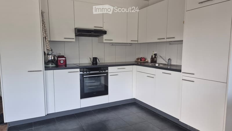 Modern kitchen with white cabinets, black countertop, stainless steel sink, and various appliances including an oven and blender.