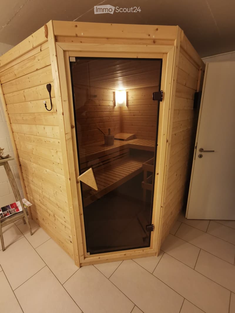 A wooden sauna with glass door, wooden benches, a small stool, and a cup inside.