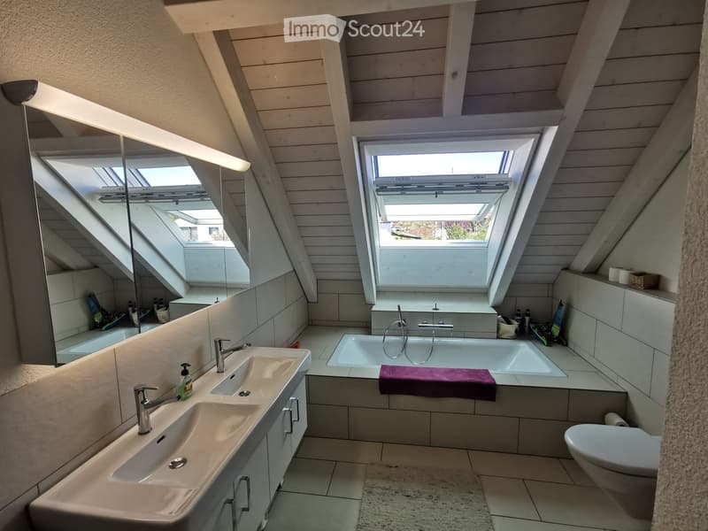 Modern bathroom with skylight windows, double sink, bathtub, toilet, and a purple towel on the edge of the tub.