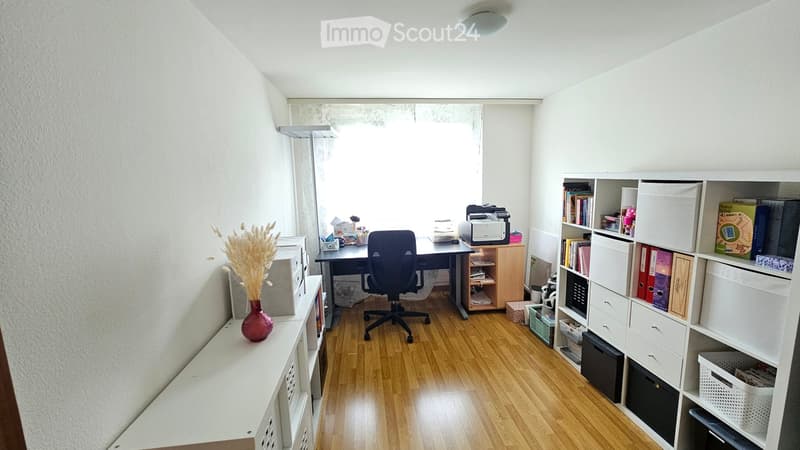 Well-lit office space with wooden flooring, a desk with a chair, a printer, a bookshelf, and a microwave on a side table.