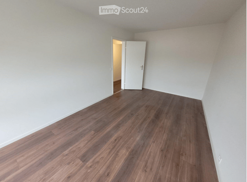 Empty room with light-colored walls and wooden flooring, featuring a white door leading to another space.