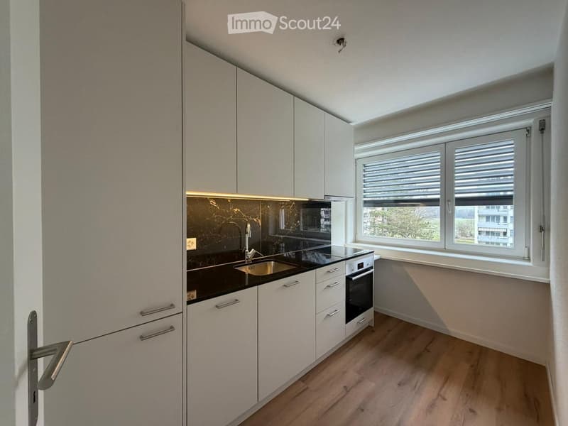 modern kitchen with white cabinets, black countertops, stainless steel sink, oven, window with blinds