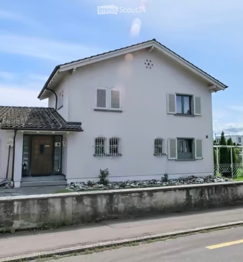 Two-story house with light pink exterior, multiple windows with shutters, and a small entrance porch.
