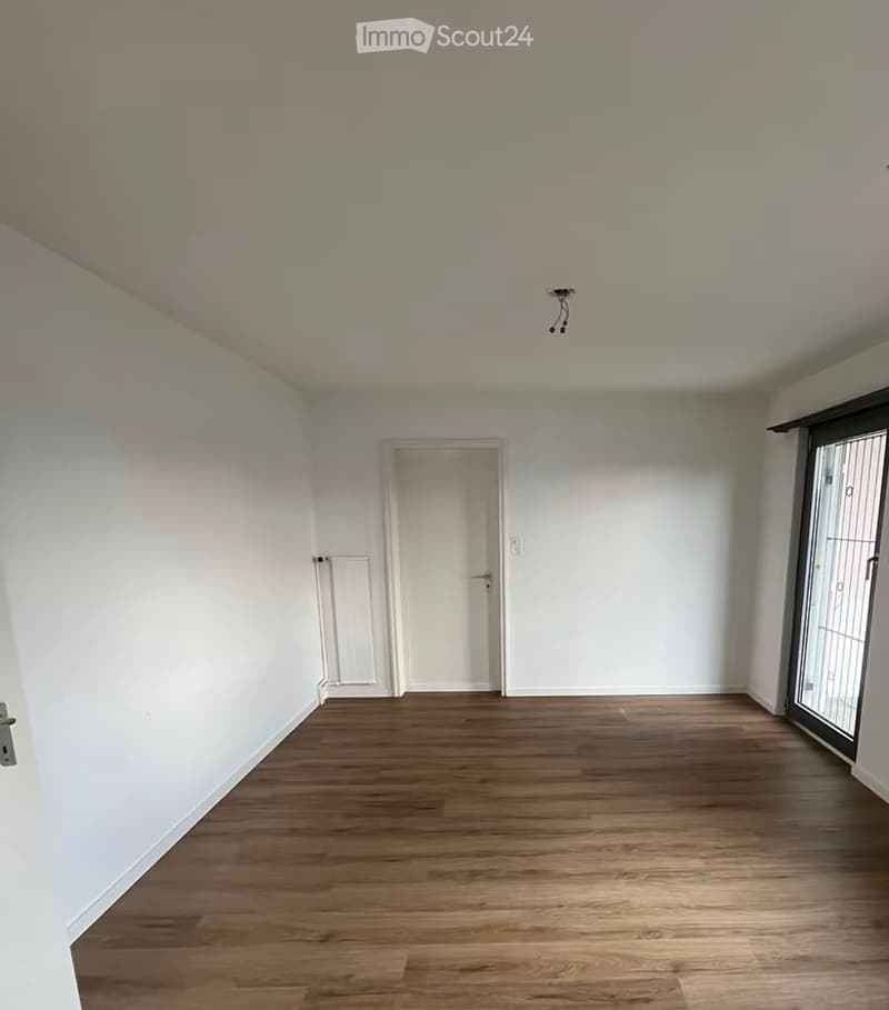 Empty room with wooden flooring, white walls, a door, and a radiator. No furniture or equipment present.
