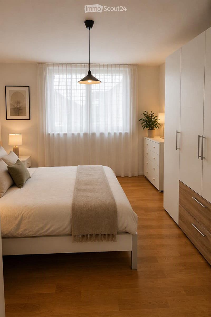 Modern bedroom with a large bed, nightstand, lamp, potted plant, and a tall cabinet with drawers. The room features wooden flooring and large windows with sheer curtains.