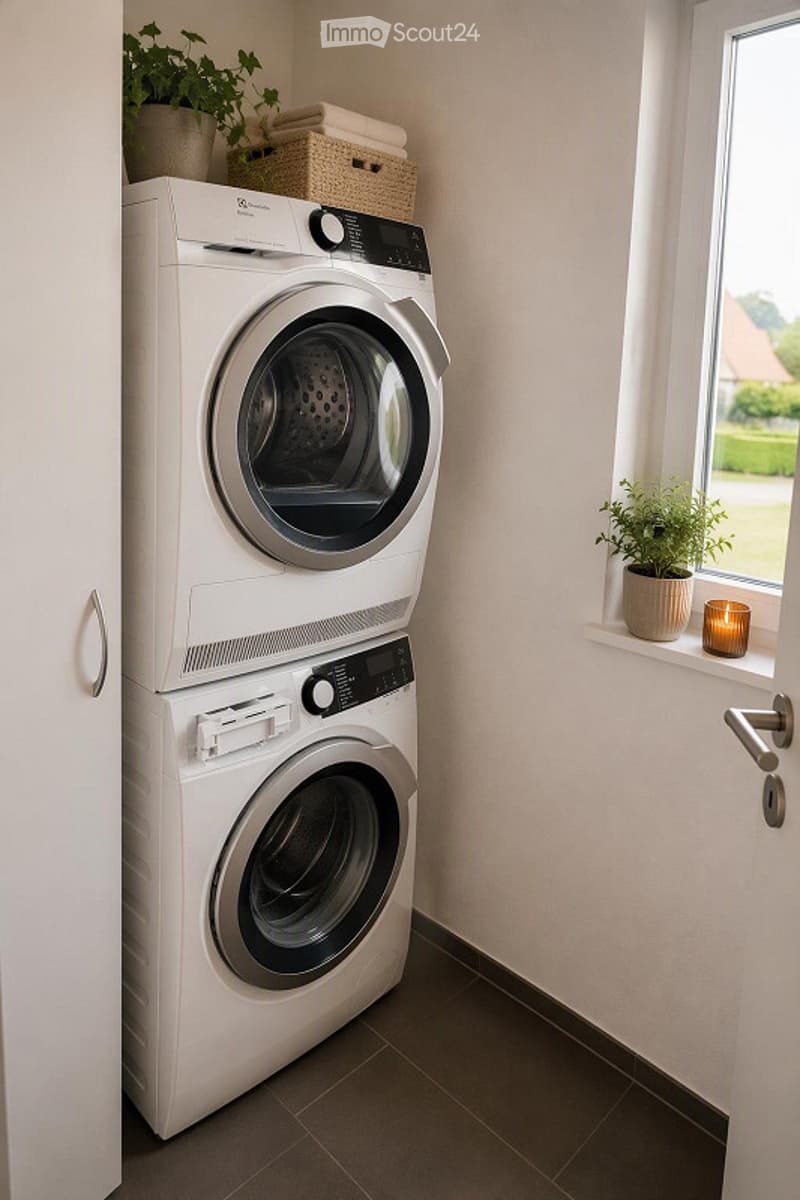 Modern bathroom with a stacked washer and dryer unit, a small potted plant on the windowsill, and a lit candle on the windowsill.