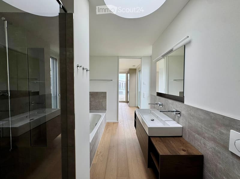 Modern bathroom with a bathtub, double sink, and large mirror. Features wooden flooring and sleek, contemporary design.