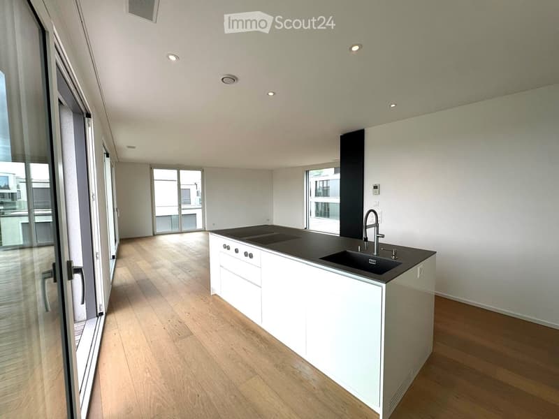 Modern kitchen with white cabinets, black countertop, and a sink. Large windows and sliding glass doors provide natural light and access to the outdoor area.