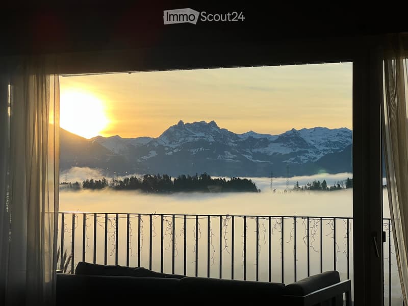 Balcony with a sofa, overlooking a mountain range at sunset with a misty valley below.