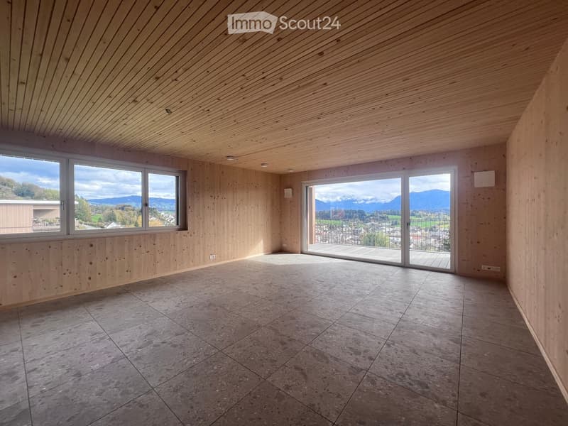 Empty room with wooden walls and ceiling, large windows, and a sliding glass door leading to a balcony with a scenic mountain view.
