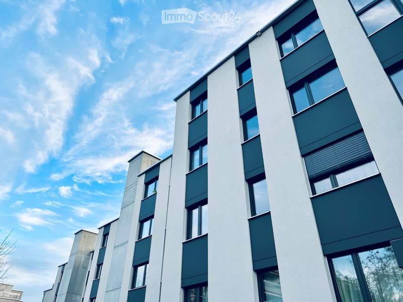 Modern multi-story building with white and green facade, large windows, and balconies.