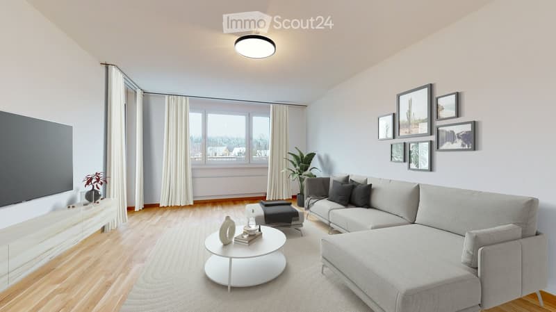 Modern living room with light grey sofa, white coffee table, ottoman, and large windows with white curtains. Features a television on a white stand, a plant, and several picture frames on the wall.
