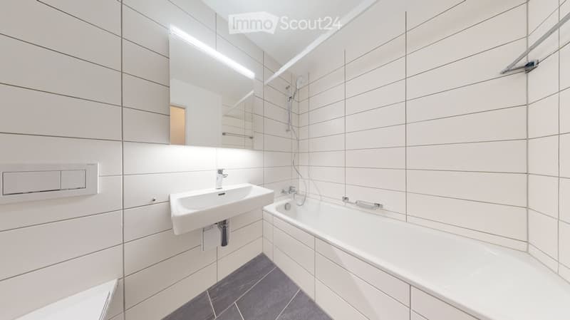 Modern bathroom with white tiles, a sink, bathtub, mirror, and showerhead.
