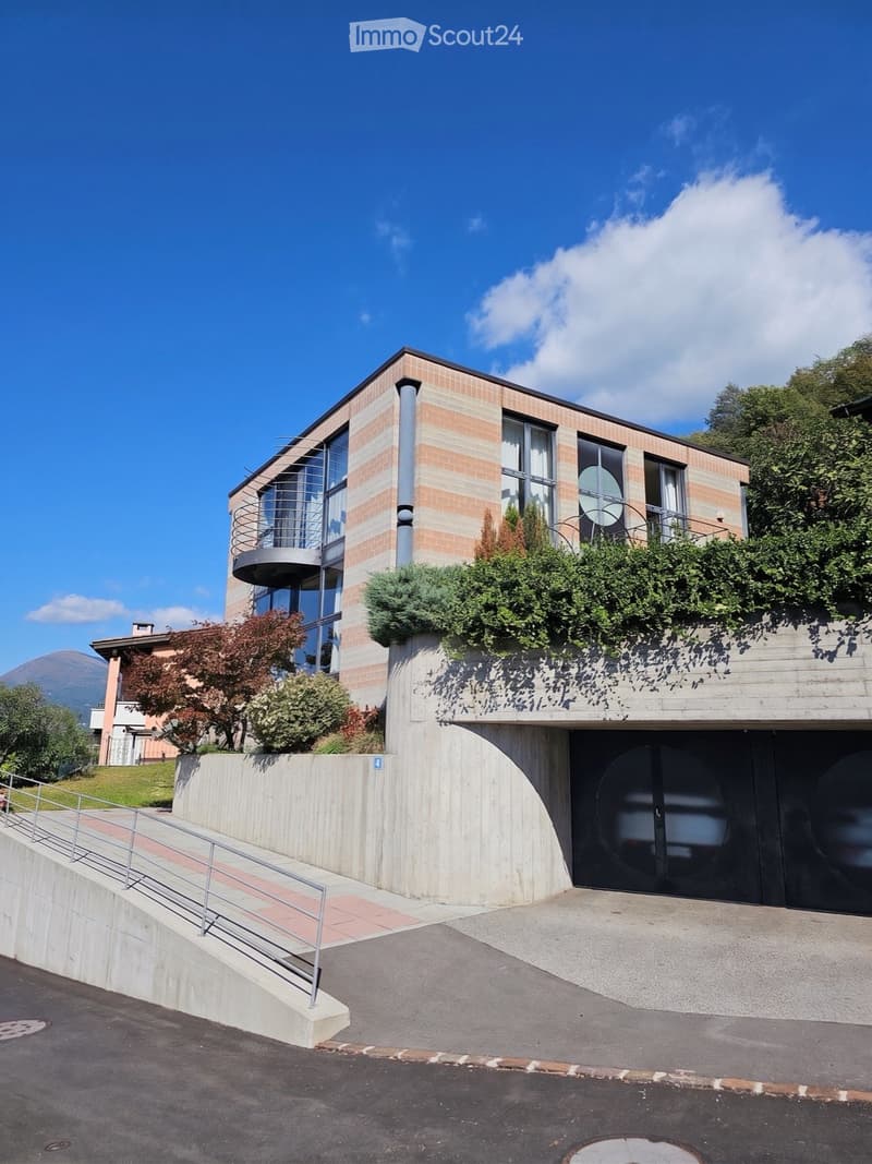 Modern two-story building with brick and glass facade, curved balcony, and landscaped rooftop garden.