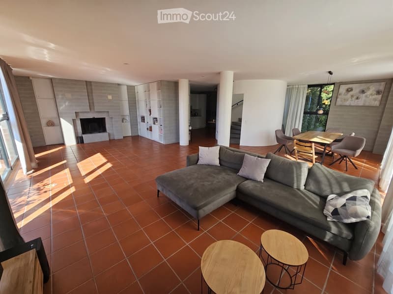 Modern living room with terracotta tile flooring, large sectional sofa, coffee table, fireplace, dining area with table and chairs, and built-in bookshelf.