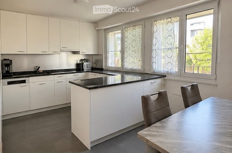 Modern kitchen with white cabinets, black countertops, a central island, and a small dining area with a table and chairs.