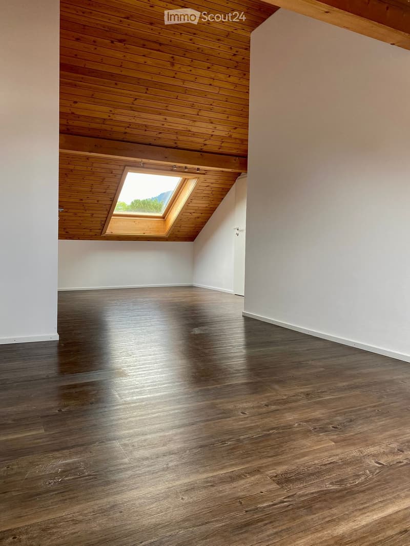 Empty room with wooden floor and white walls, featuring a skylight window in the sloped wooden ceiling.