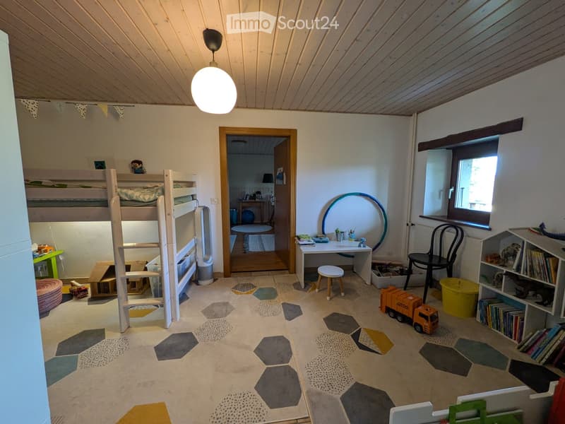 Bright, cozy bedroom with a bunk bed, desk, chair, and various toys. Features a large window, a round mirror, and a colorful geometric rug.