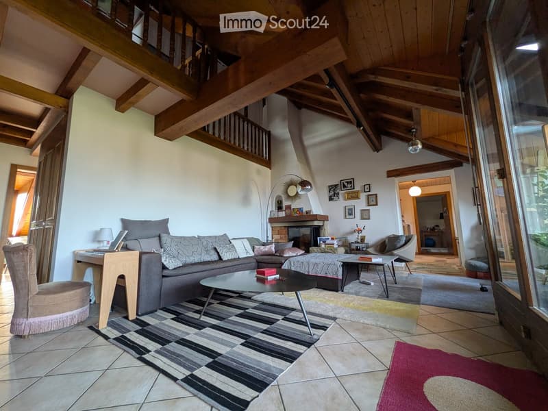 Living room with exposed wooden beams, a grey sectional sofa, coffee table, fireplace, and a large window with a view.