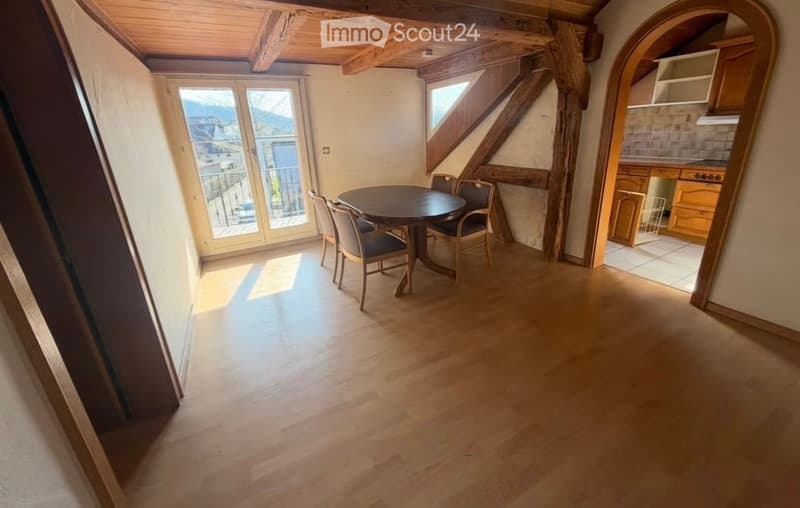 Bright dining area with wooden floor, exposed wooden beams, large windows offering a scenic mountain view, and a round dining table with chairs.