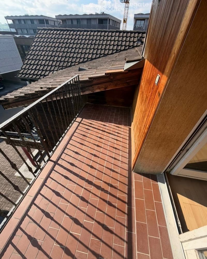 Balcony with brick tiles, metal railing, and view of neighboring buildings and rooftops.