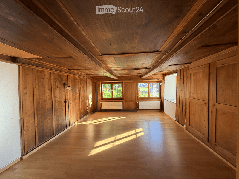 Empty room with wooden walls, ceiling, and floor, featuring large windows and radiators, with natural light streaming in.