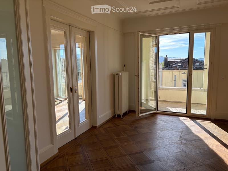 Empty room with wooden flooring, large glass doors leading to a balcony, and a radiator on the wall.