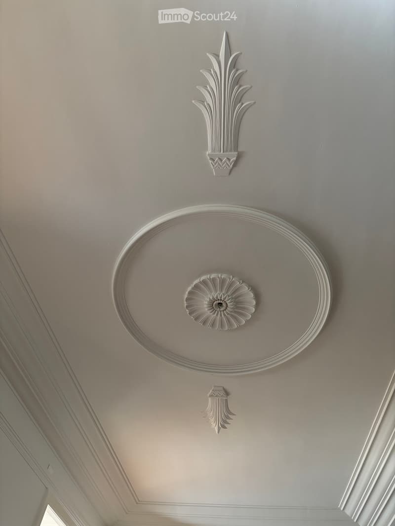 Ornate ceiling with decorative plaster moldings and floral motifs, featuring a central circular medallion and surrounding detailed designs.
