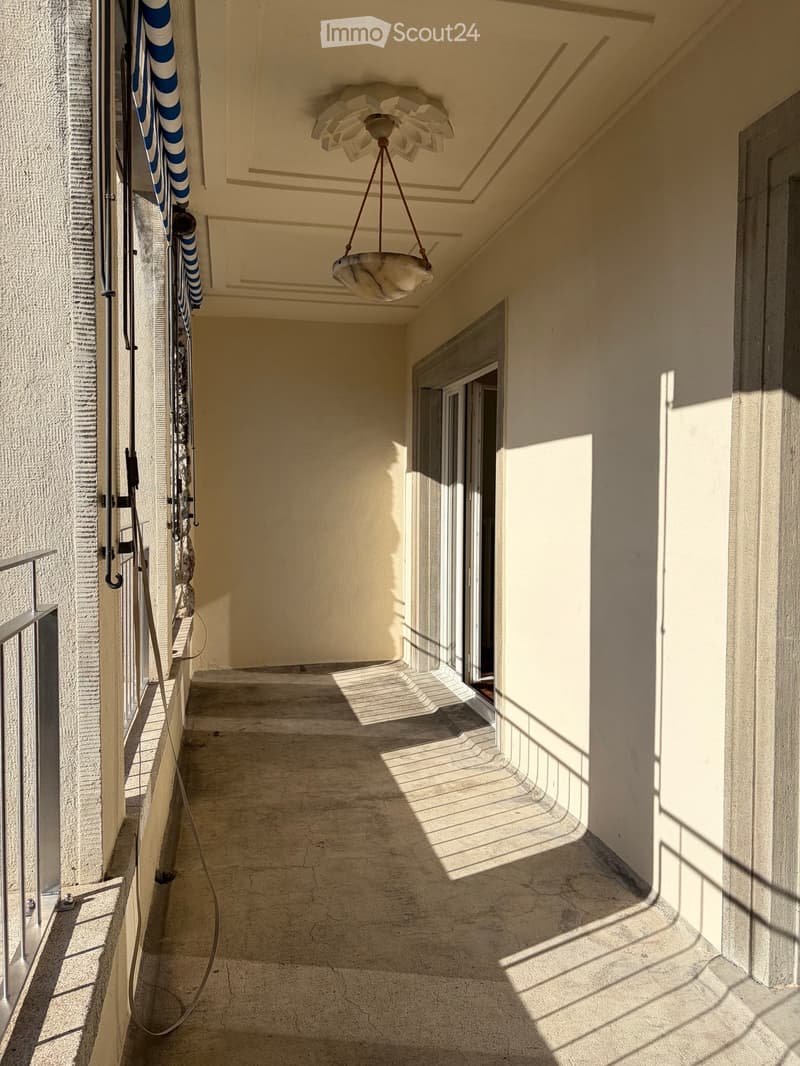 Balcony with beige walls, a hanging light fixture, and a metal railing. A swimming pool ladder is visible on the left side.