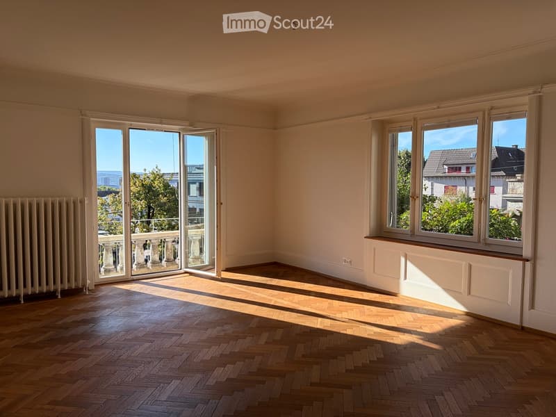 Empty room with wooden herringbone flooring, large windows, and a sliding glass door leading to a balcony.