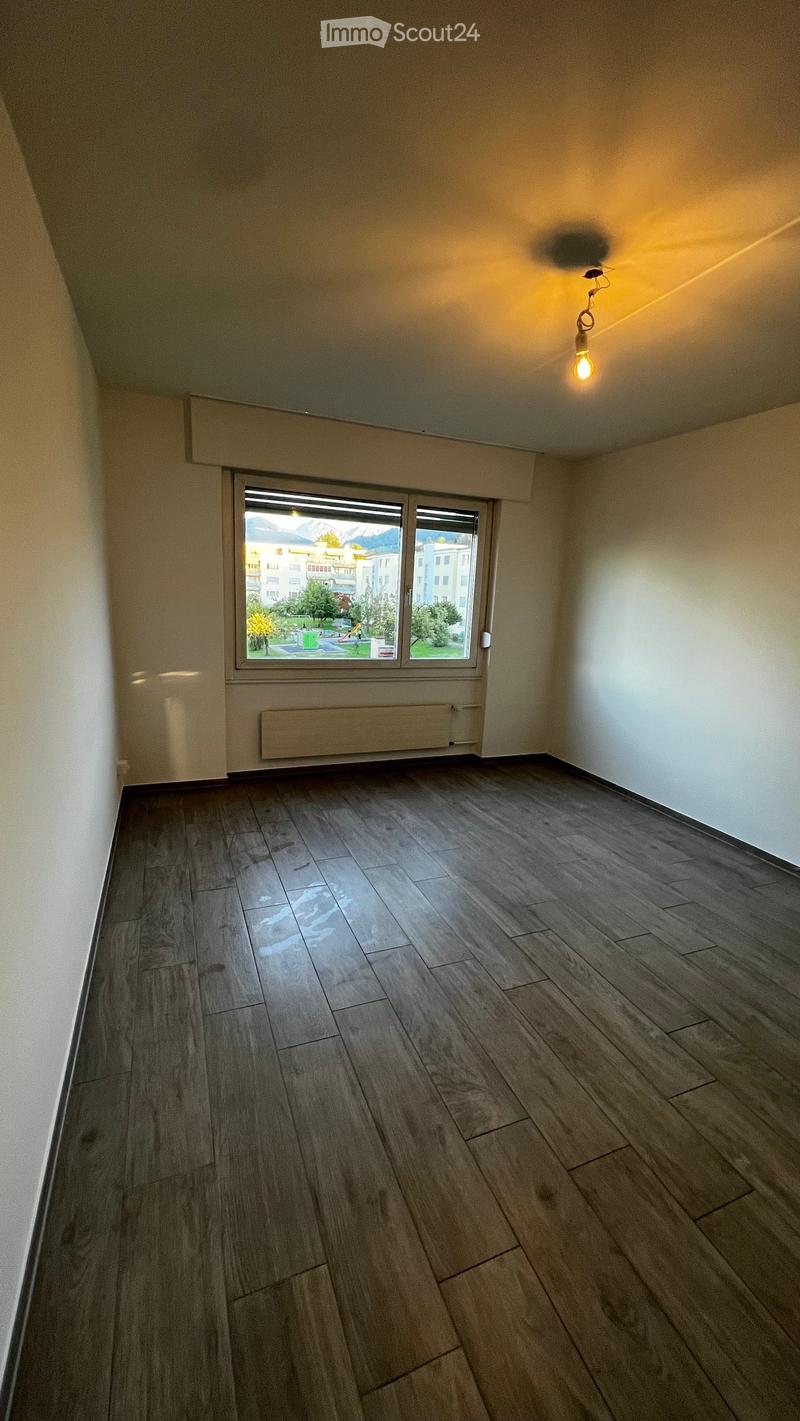 Empty room with wooden flooring, white walls, and a large window offering a view of the outside area.