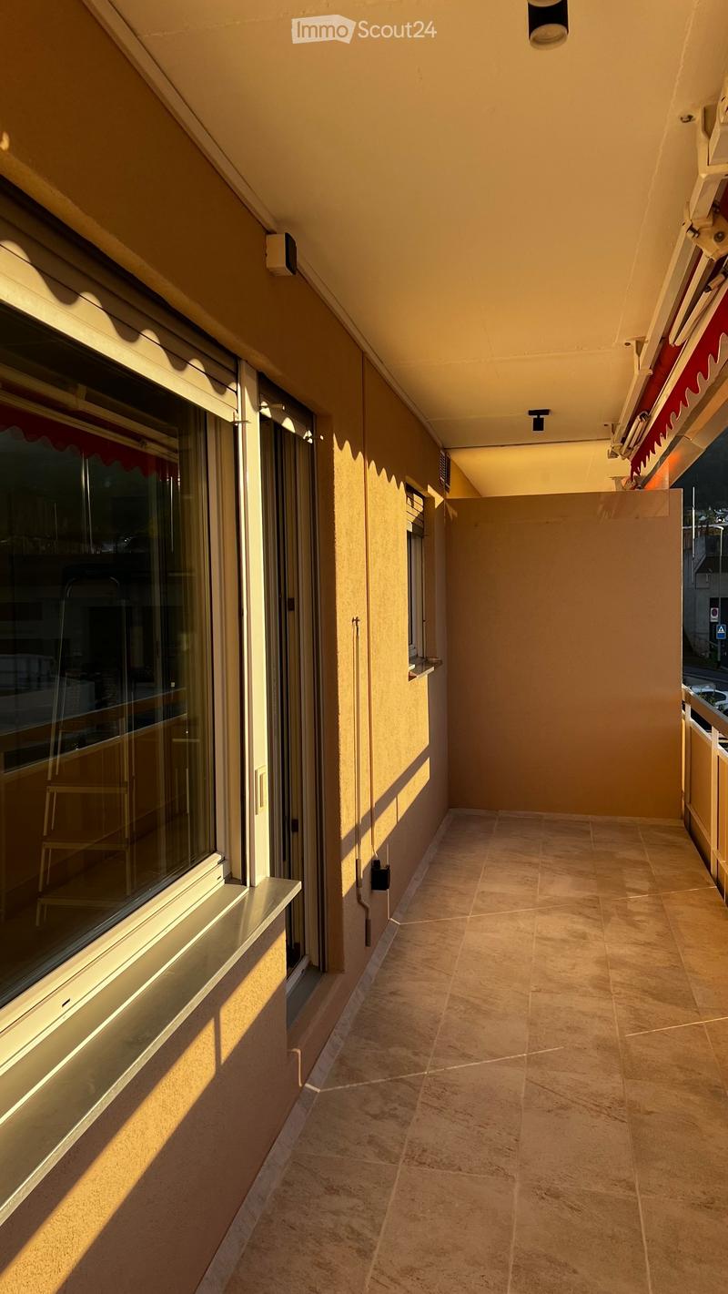 Balcony with tiled floor, beige walls, large windows, and a covered section with a red awning.