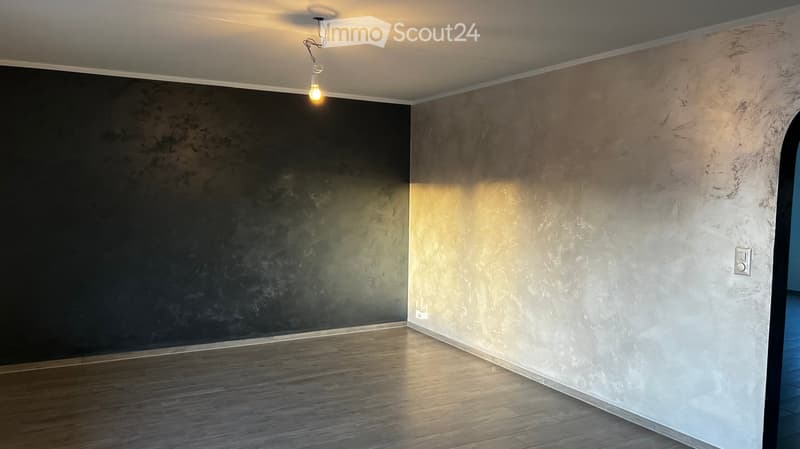 Empty room with wooden flooring, two walls in contrasting colors, and a single hanging light fixture.