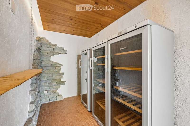 A small, well-lit room with a stone wall, wooden ceiling, and a built-in wine refrigerator with wooden shelves.