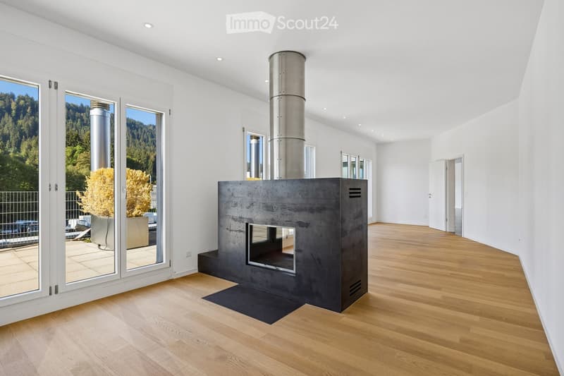 Modern living room with a sleek concrete fireplace, large windows offering a scenic view, and light wooden flooring.