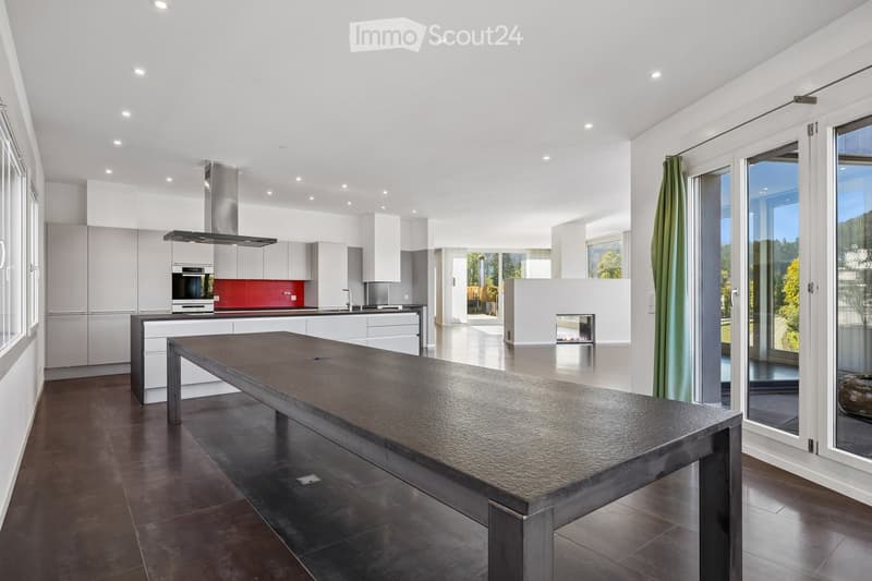 Modern kitchen with white cabinets, stainless steel appliances, a large central island, and a fireplace in the background.