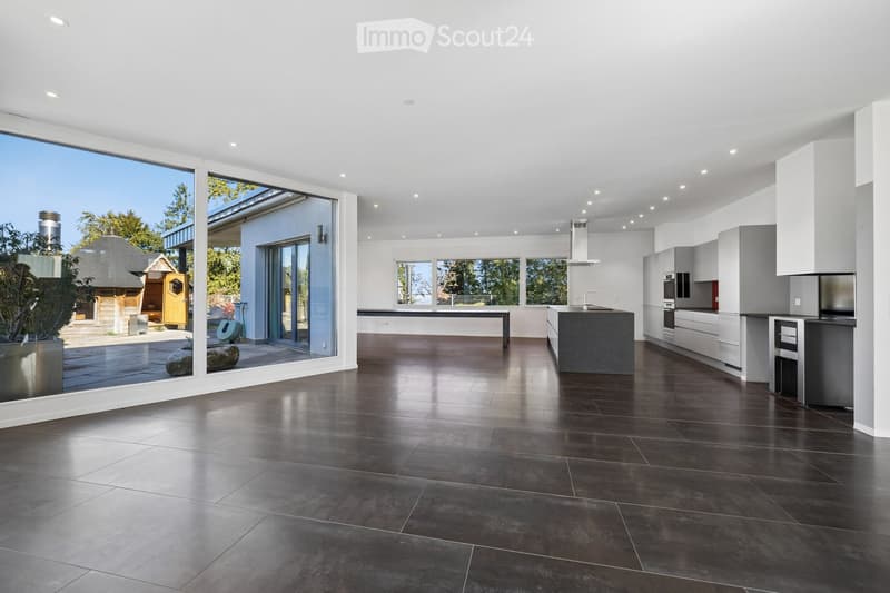 Modern kitchen with dark tiled flooring, white cabinets, a central island, and large windows overlooking an outdoor area.