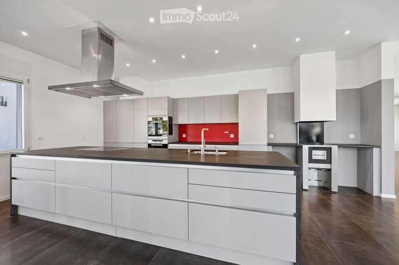 Modern kitchen with white cabinets, dark countertops, a central island, and a stainless steel range hood.