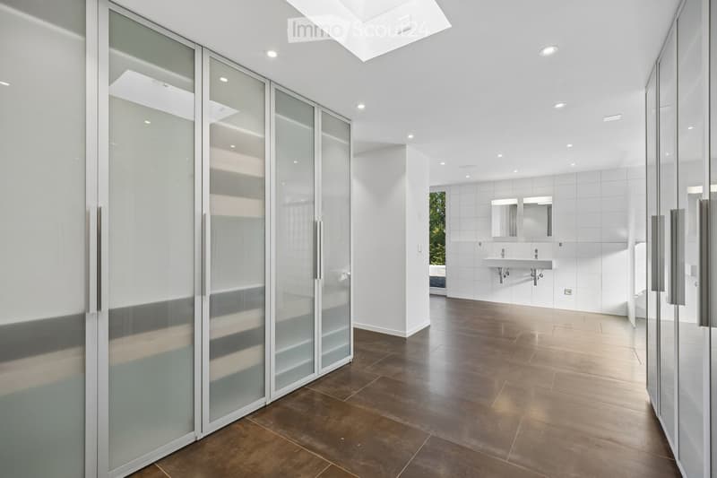 Modern bathroom with sleek glass partitions, a double sink, and large mirrors. The space features a polished dark wood floor and recessed lighting.