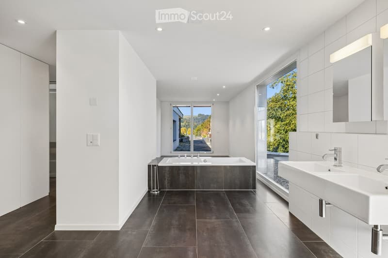 Modern bathroom with dark tiled floor, white walls, large windows, bathtub, sink, and mirror.