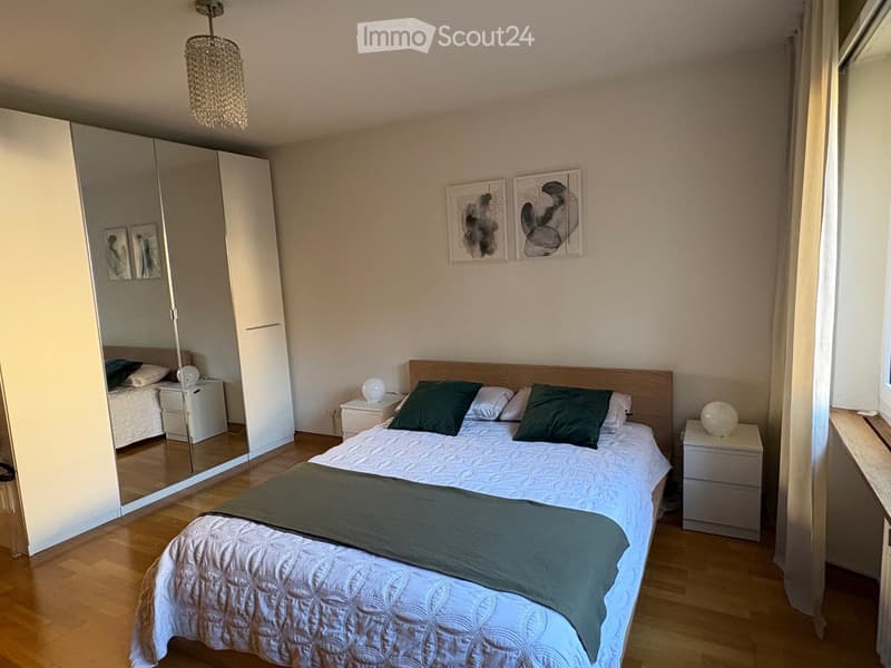Modern bedroom with a large bed, nightstands, a wardrobe with a mirror, and decorative artwork on the wall.