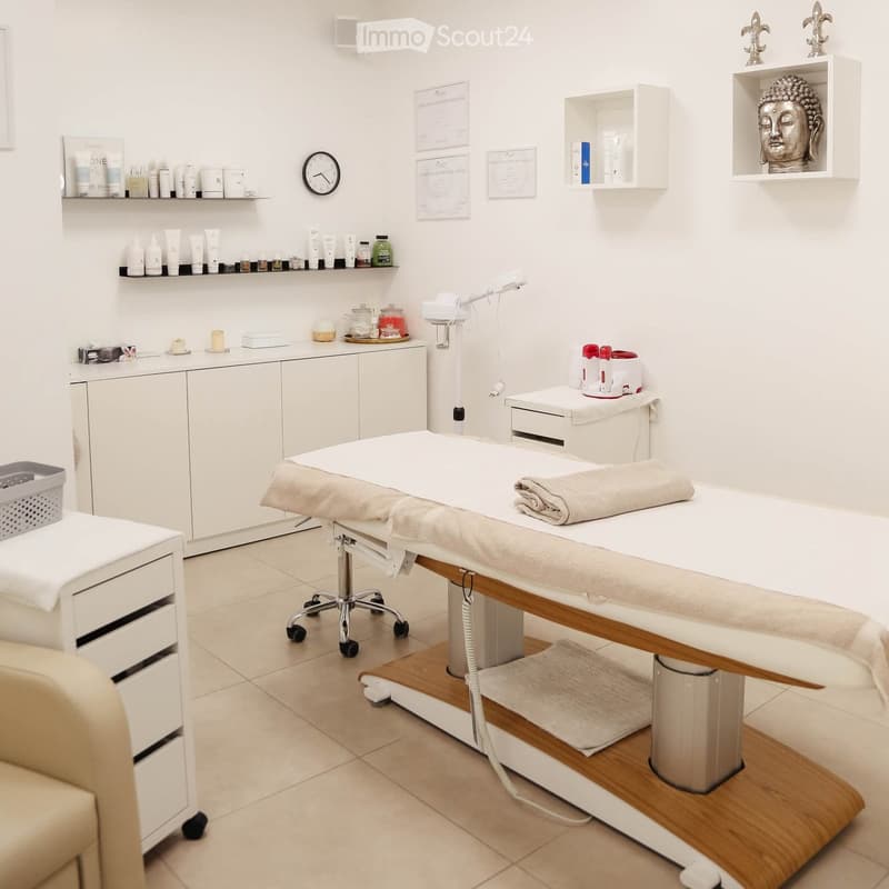 A clean, well-organized spa treatment room with a white treatment table, shelves holding various products, a cabinet, and a small statue on a shelf.