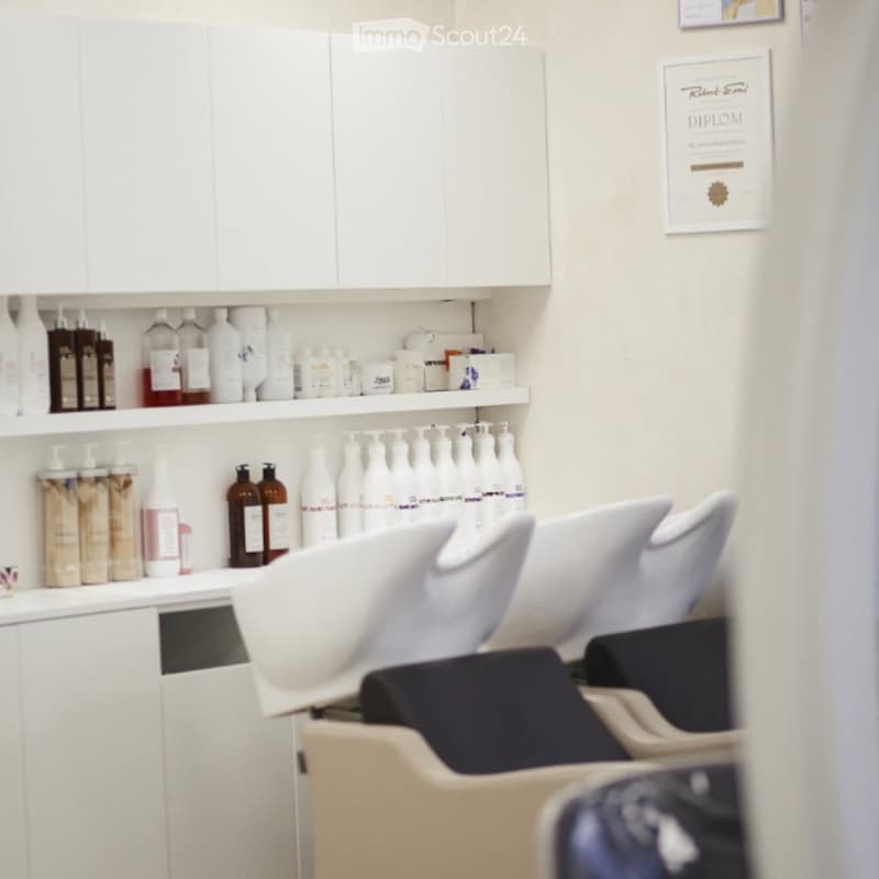 A modern, well-organized salon with white cabinets, shelves filled with various hair care products, and multiple salon chairs.
