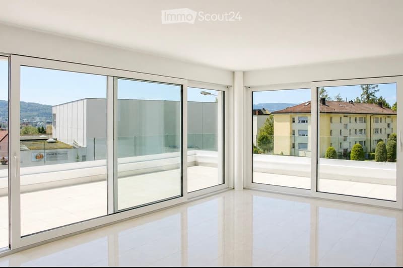 Bright, empty room with large glass sliding doors opening to a balcony, offering a scenic view of buildings and greenery.