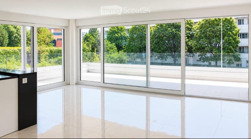 Bright, empty room with large glass sliding doors leading to a balcony, white tiled floor, and modern white walls.