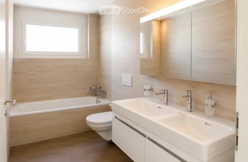 Modern bathroom with a bathtub, toilet, double sink, large mirror with built-in lighting, and sleek chrome fixtures.