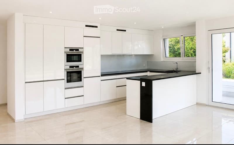 Modern kitchen with white cabinets, stainless steel appliances, black countertops, and a central island.
