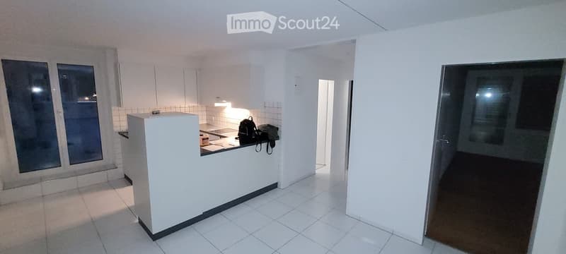 Empty kitchen area with white tiled floors, white cabinets, and a counter. No furniture or appliances are present.