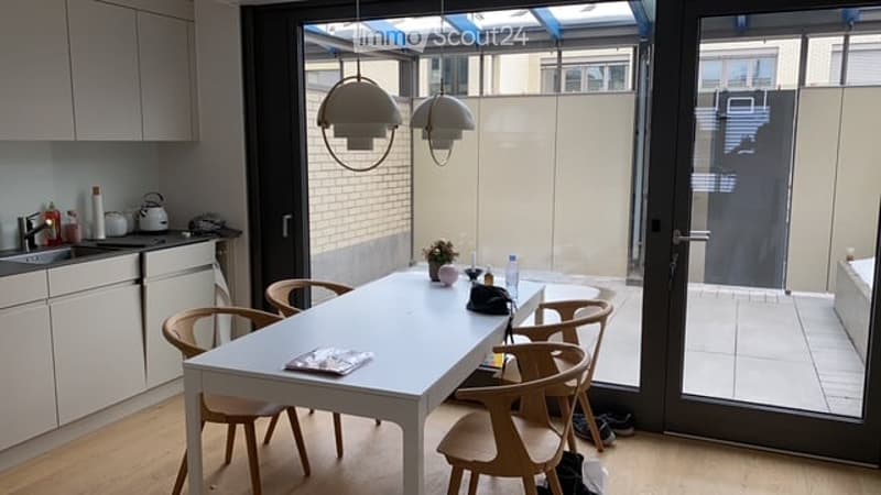 Modern kitchen with a white dining table and chairs, grey cabinets, and a large window overlooking a patio area.