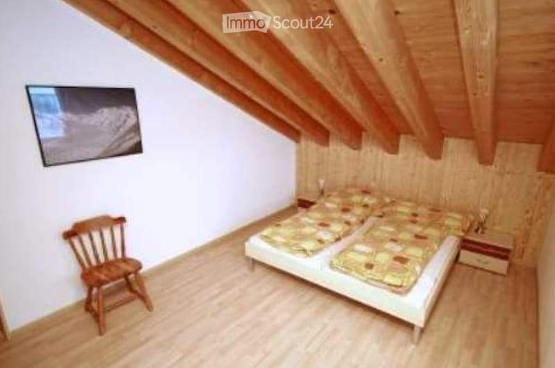 Cozy attic bedroom with wooden slanted ceilings, two single beds, a wooden chair, and a nightstand.